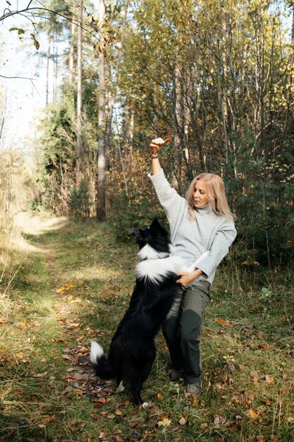 Happy woman and black and white border collie dog in autumn forest