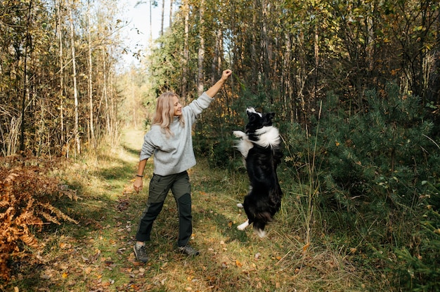 Happy woman and black and white border collie dog in autumn forest