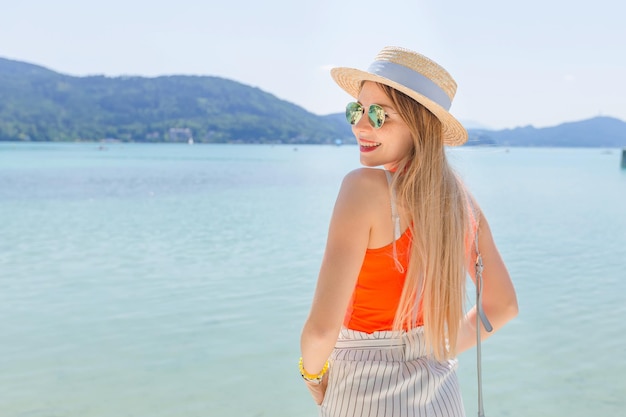 Happy woman in boater and sunglasses near the lake with mountain