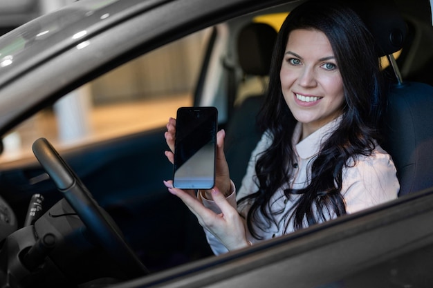 Happy woman buyer examines her new vehicle in car dealership