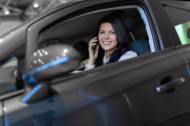 Счастливый покупатель женщины сидя в ее новом автомобиле в автосалоне