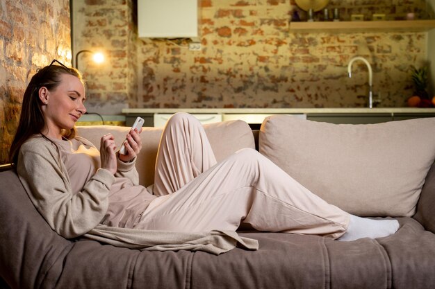 Happy woman checks social networks while keeping her smartphone at home A smiling young woman using a mobile phone app shopping online ordering delivery resting on the couch