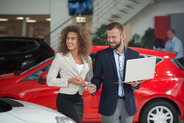 Donna felice che sceglie automobile con il gestore del concessionario auto.