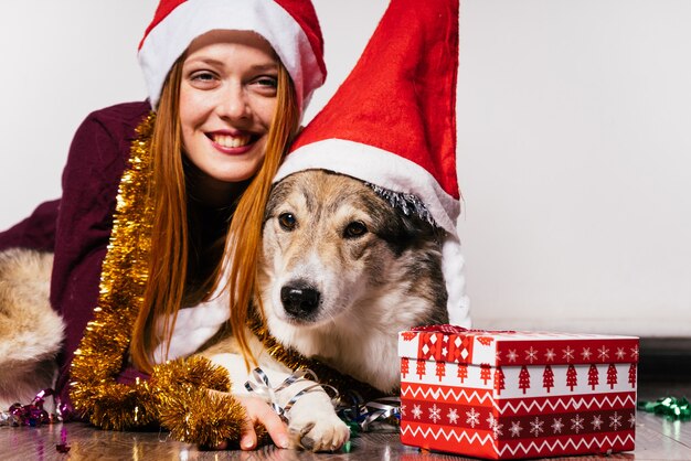 Happy woman in a Christmas hat hugs a dog on a gift background