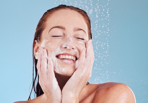 Foto donna felice che pulisce viso e sapone per doccia di bellezza e igiene con toelettatura su sfondo blu sostenibilità del modello femminile e goccia d'acqua con dermatologia facciale e cura della pelle in studio