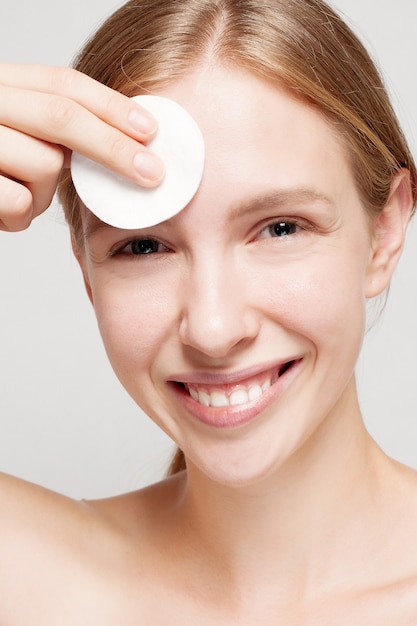 Happy woman cleaning her face with cotton pads