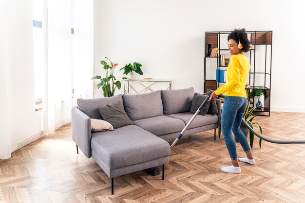 Happy woman cleaning home with vacuum cleaner and listening music