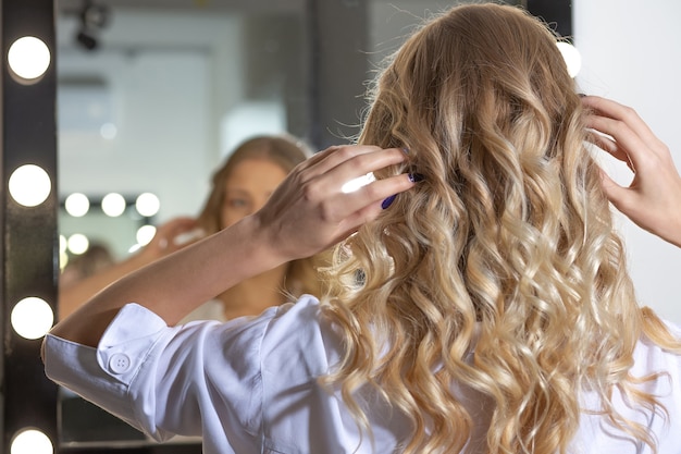 Happy woman client looking to her reflection in the mirror after hairstyling at beauty salon