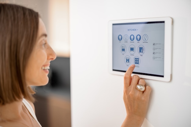 happy woman controlling smart devices using control panel at kitchen