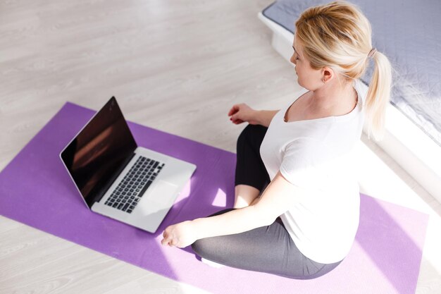 Happy woman doing exercise while watching workout video on laptop at home