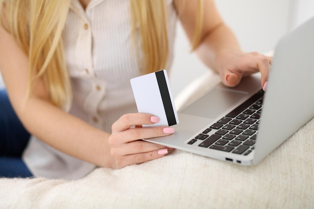 Donna felice che fa shopping online a casa. primo piano di una mano che tiene una carta di credito accanto a un computer portatile.