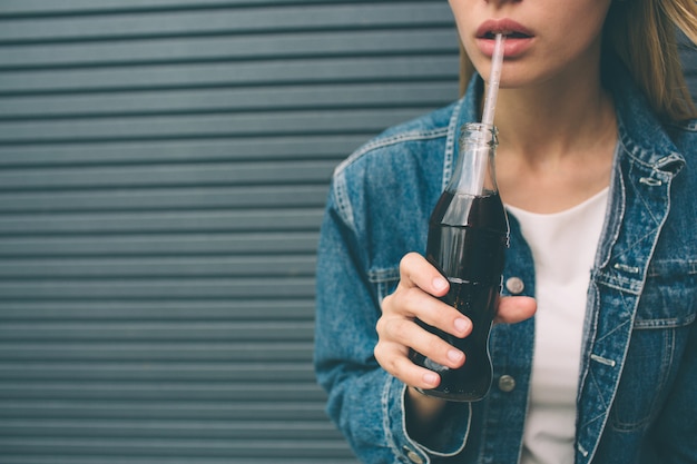 happy woman drinking with straw near the gray wall