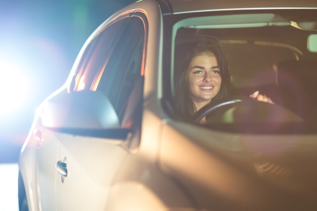 幸せな女性は車を運転します。夕方の夜