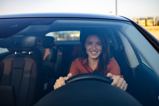 Happy woman driving a car and smiling Cute young success happy brunette woman is driving a car Portrait of happy female driver steering car with safety belt