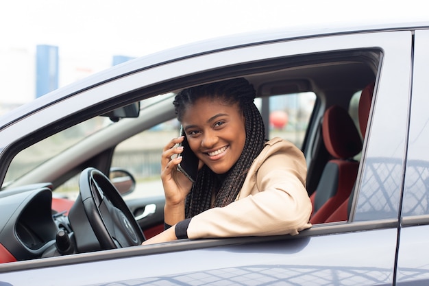 Donna felice alla guida di un'auto con un telefono, afro-americano