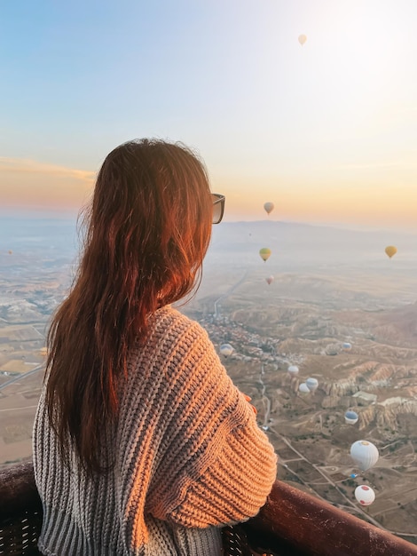 Photo happy woman during sunrise watching hot air balloons show from a basket in the sky in cappadocia turkey