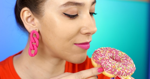 Foto donna felice che mangia una deliziosa ciambella rosa. compleanno.