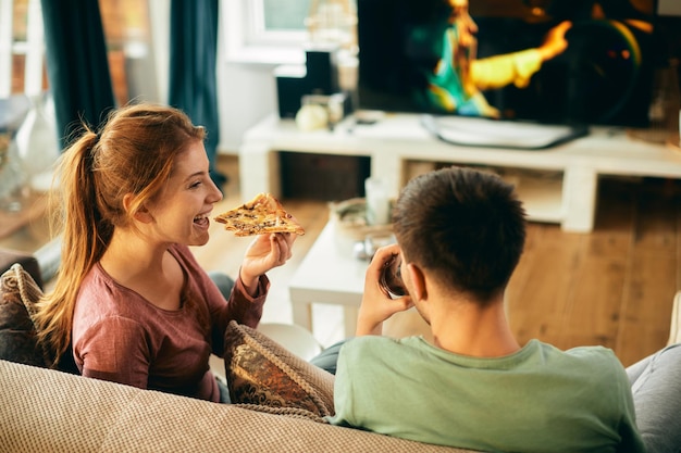 Happy woman eating pizza while watching TV with her boyfriend at home