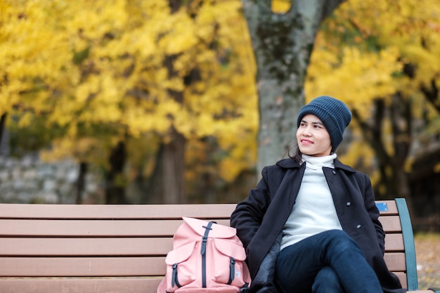 Happy woman enjoy at the park outdoor in Autumn season, Asian traveler in coat and hat against Yellow Ginkgo Leaves background