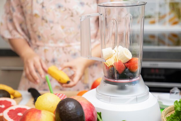 La donna felice si diverte a preparare frutta appena spremuta con verdure per preparare frullati per colazione insieme in cucina. dieta e concetto di salute.