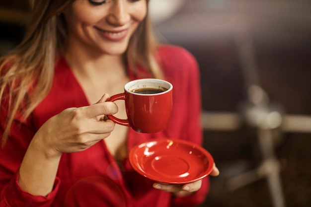 A happy woman enjoying cup of coffee while standing next to a coffee roasting machine