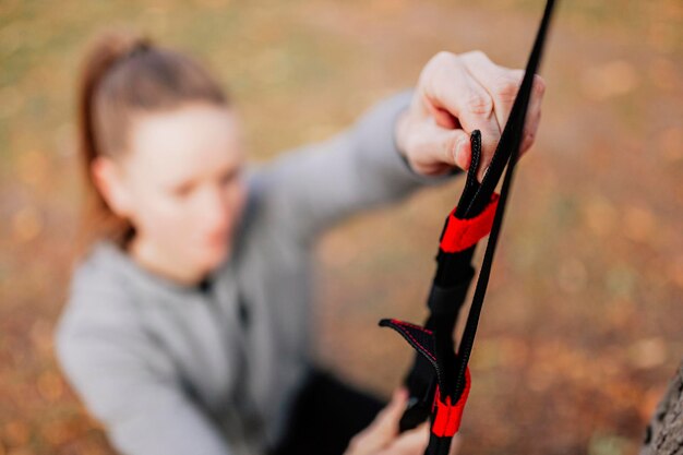 Happy woman exercising with straps while standing by tree