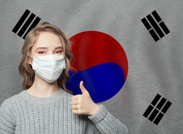 Photo happy woman in face mask holding thumb up on korea flag background flu epidemic and virus protection concept