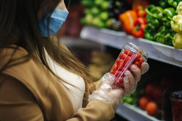Счастливая женщина в маске для лица, принимая свежие помидоры черри, стоя у продуктов в супермаркете