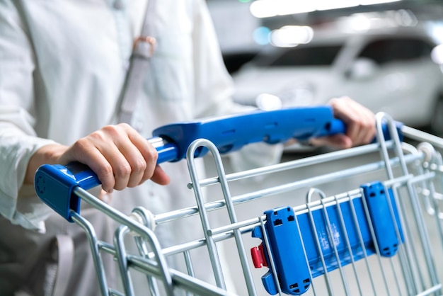 Carrello o carrello della spesa femminile della donna felice nel parcheggio dell'automobile della marca fresca nel deposito del supermercato