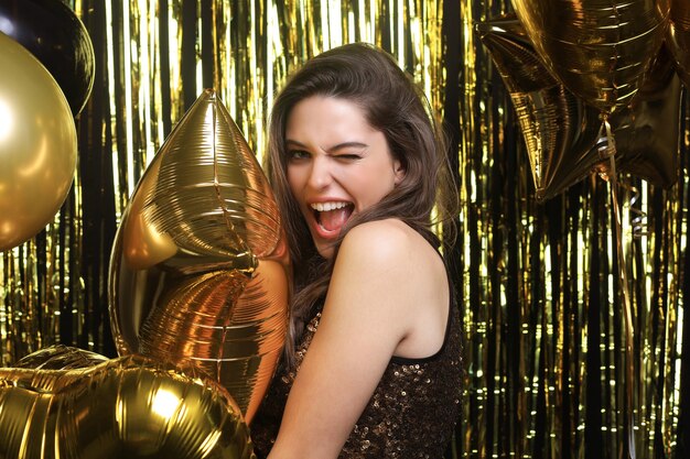 Happy woman in festive outfit holding gold balloons.