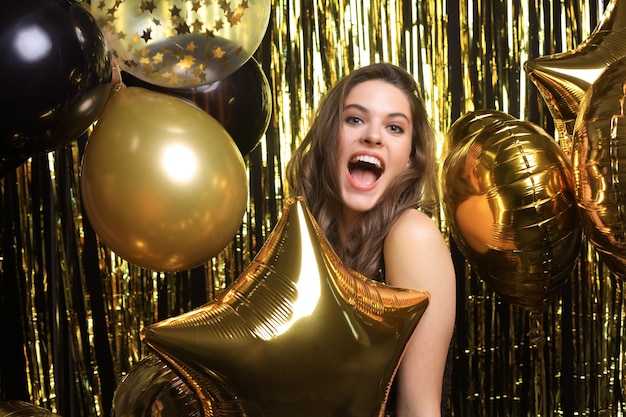 Happy woman in festive outfit holding gold balloons.