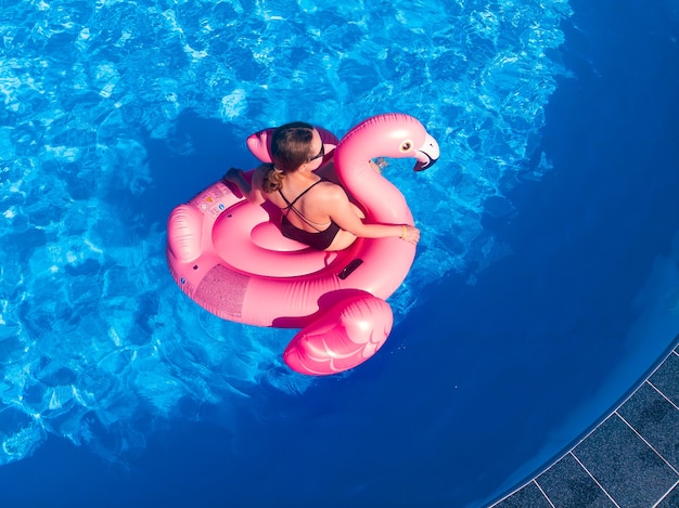 Happy woman on flamingo pool float in pool in the hotel, drone aerial view