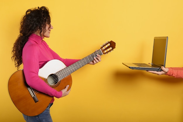 Happy woman follows a guitar lesson online.