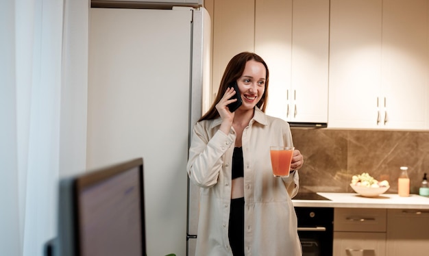 Happy woman freelancer in casual clothes talking phone with\
friends standing on home kitchen during work brake hi nice to meet\
you