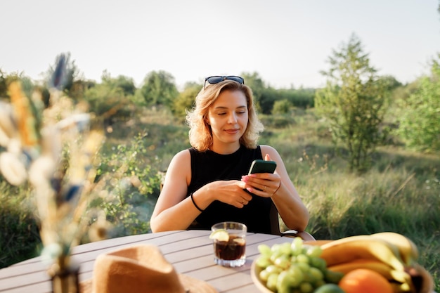 Happy Woman freelancer use phone and drinking cocktail call while relaxing on cozy glamping tent in sunny day Luxury camping tent for outdoor summer holiday and vacation Lifestyle concept