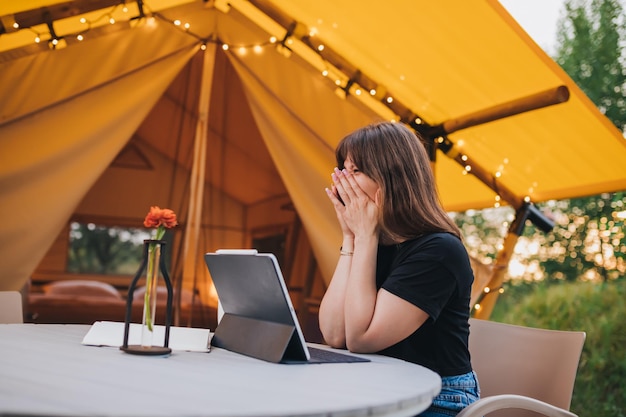 Happy Woman freelancer using a laptop on a cozy glamping tent in a sunny day Luxury camping tent for outdoor summer holiday and vacation Lifestyle concept