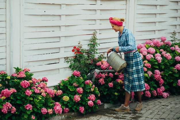 Happy woman gardener with flowers Flower care and watering soils and fertilizers Greenhouse flowers woman care of flowers in garden hydrangea Spring and summer hydrangea plantation