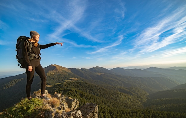 The happy woman gesturing on the sunny mountain