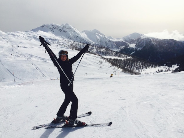 Photo happy woman gesturing while skiing on snowy field by mountains against sky