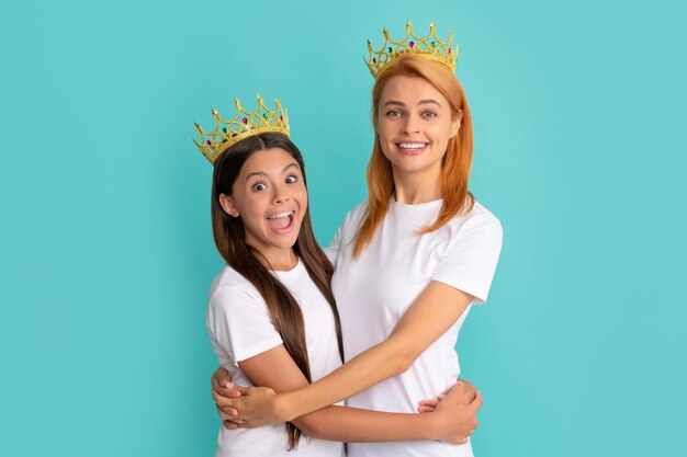 Happy woman and girl child in crowns hug smiling blue background mother