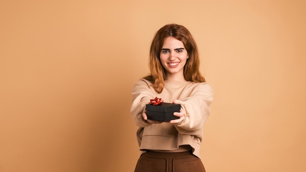 Happy woman giving gift box in brown studio