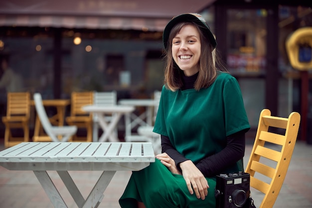 Happy woman in green dress in urban city is sitting near cafe