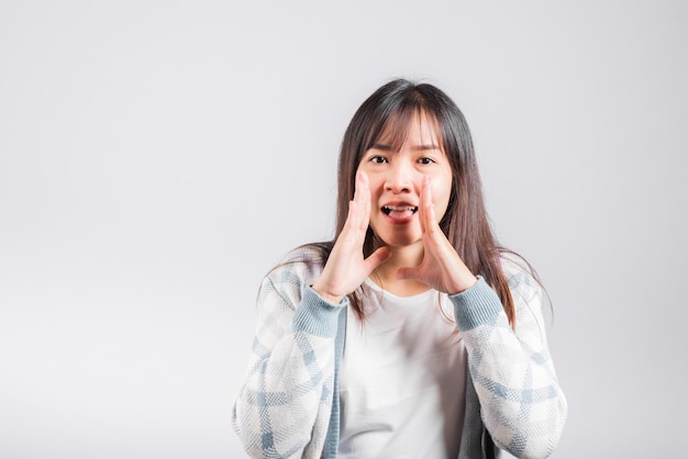 행복한 여성이 입에 손을 대고 속삭이는 비밀 소문을 말하고, 아시아의 아름다운 젊은 여성이 가십을 전하고, 복사 공간이 있는 흰색 배경에 격리된 스튜디오 샷