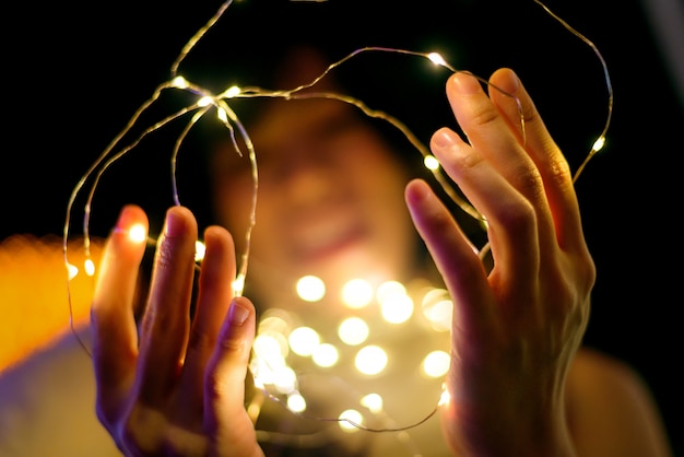 Foto la donna felice passa la tenuta della luce di natale gialla, fondo del bokeh