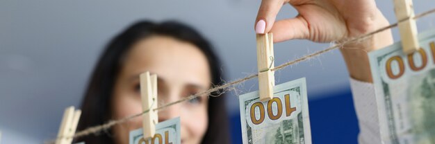 Счастливая женщина вешает чистые доллары на прищепки, чтобы высушить концепцию отмывания грязных денег