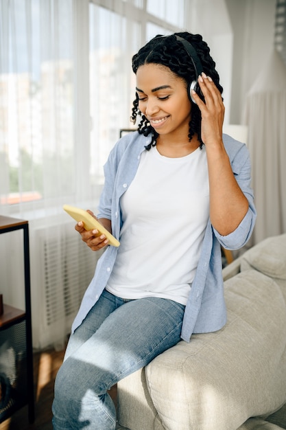 Happy woman in headphones listen to music from mobile phone. Pretty lady in earphones relax in the room, female sound lover resting