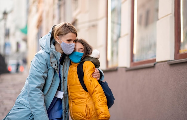 Happy woman healthcare worker outdoors in town hugging schoolgirl daughter coronavirus concept