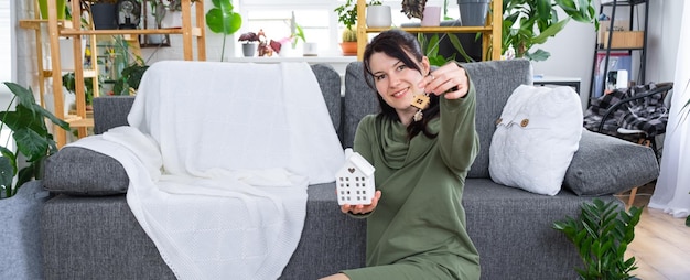 A happy woman in her house holds in her hands a miniature figure of a house and key in the interior Dream house project real estate purchase insurance mortgage rent reservation