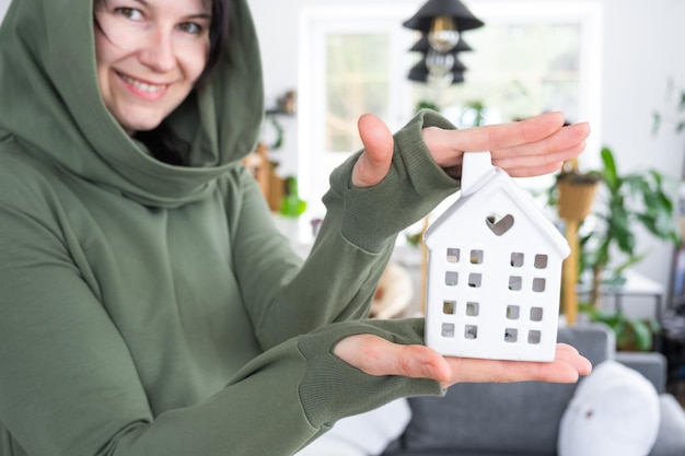 A happy woman in her house holds in her hands a miniature figure of a house and key in the interior Dream house project real estate purchase insurance mortgage rent reservation