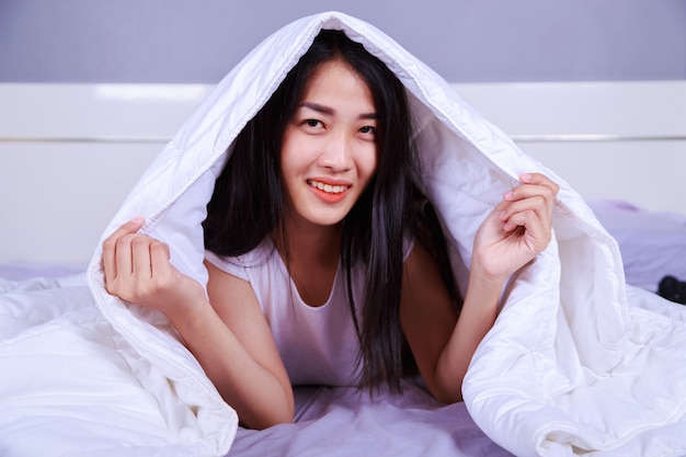 happy woman hiding under blanket on bed in the bedroom